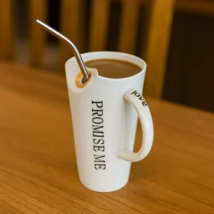 Romantic ceramic mug with “Promise Me” text filled with coffee on wooden table.