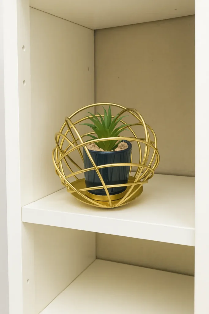 Artificial plant in golden orb metal holder placed on white shelf
